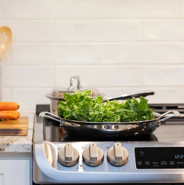 A sauté pan on a stove with kale cooking.