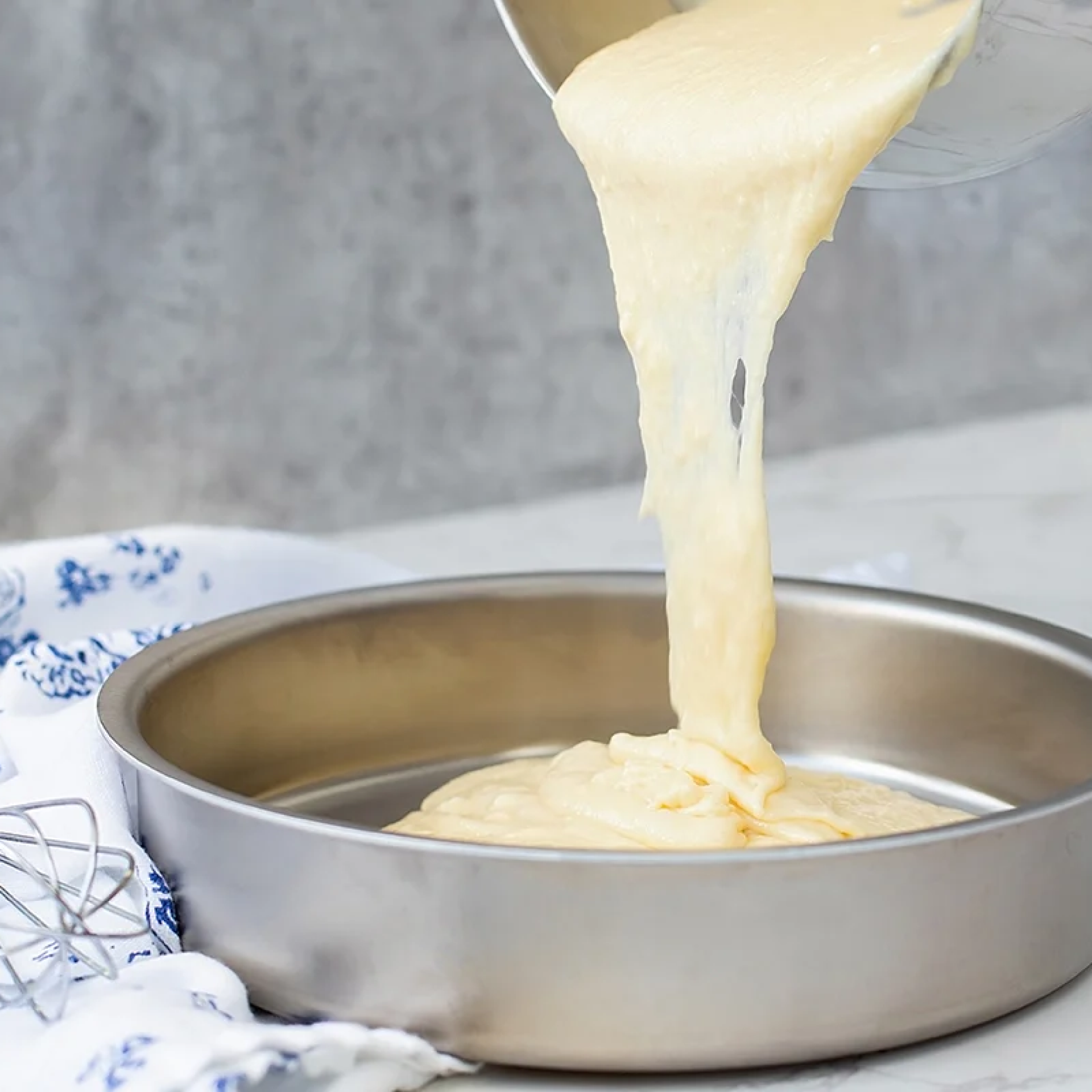 Batter being poured into a round cake pan on a marble surface
