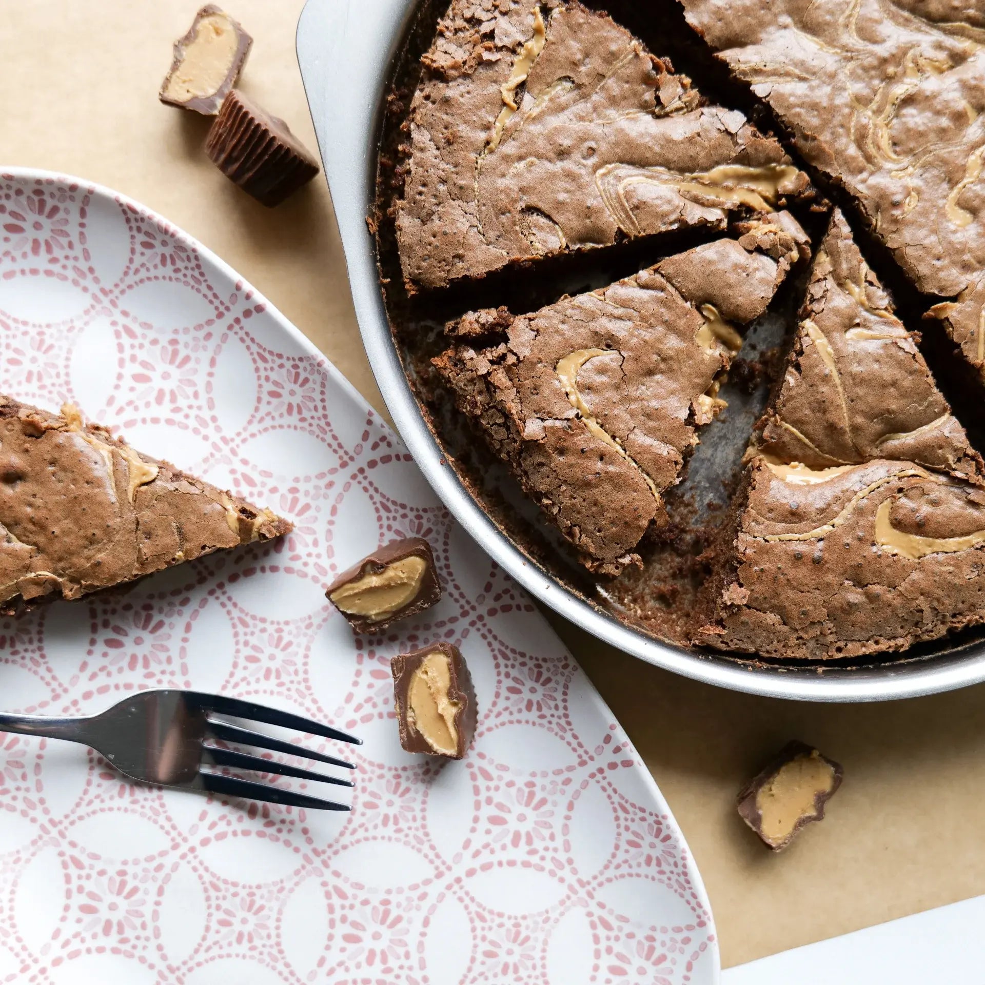 Chocolate cake with peanut butter swirls in a round pan, with a slice removed, on a patterned plate with a fork.