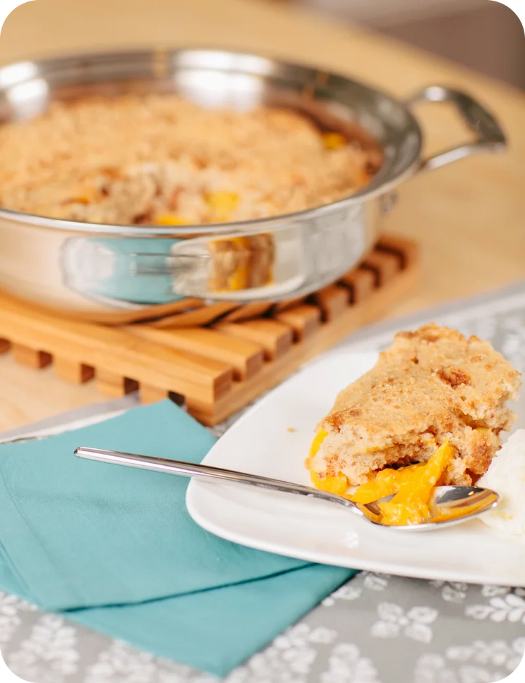 Peach cobbler in a baking dish with a slice on a plate and a fork.