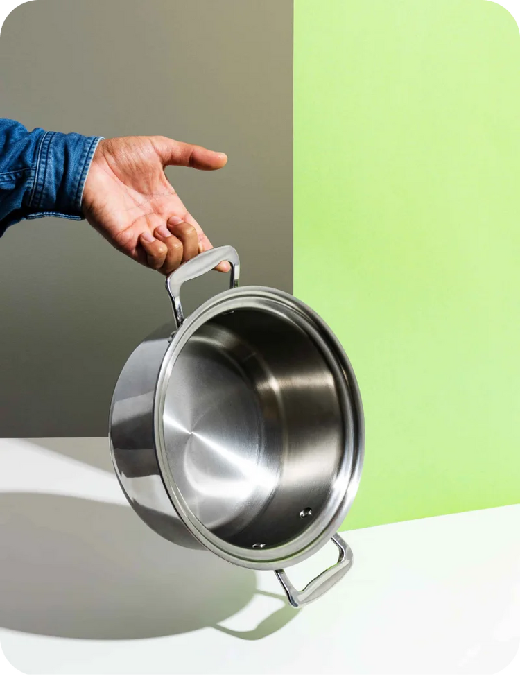 Hand holding a stainless steel pot against a green and gray background