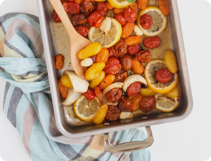 Overhead view of 9 x 13 Bake and Roast Pan with handles showing roasted cherry tomatoes, lemon, and garlic on a striped cloth