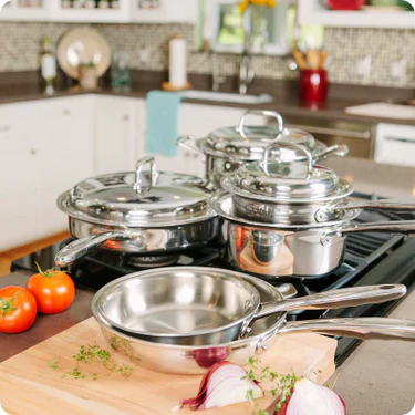 Set of stainless steel cookware on a kitchen counter with tomatoes and onions.