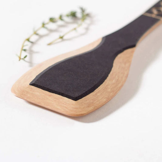 Frank Lloyd Wright Paddle with a wooden handle and black head, placed on a light background with a sprig of thyme