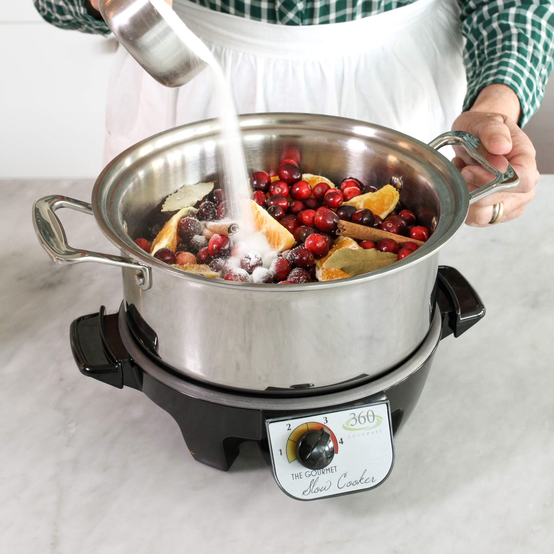 A person adding sugar to a slow cooker filled with fruits and spices.
