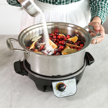 A person adding sugar to a slow cooker filled with fruits and spices.