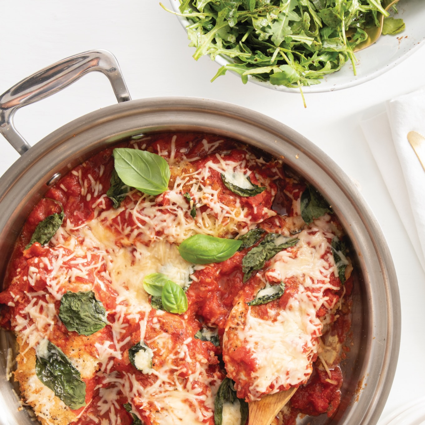 Baked chicken with tomato sauce and cheese, garnished with basil, served with a side salad.