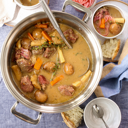 A pot of beef stew with vegetables and herbs, served with bread.