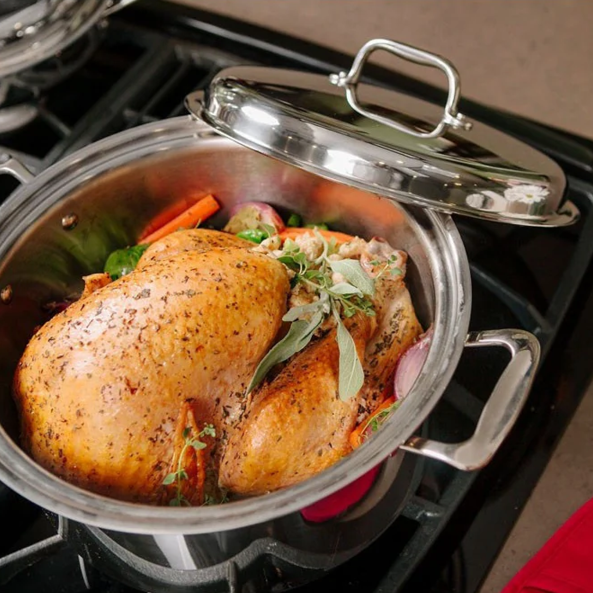 A stainless steel pot with a roasted chicken and vegetables, covered with a lid.