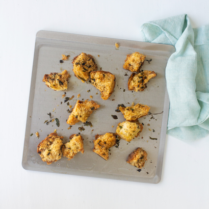 Top view of stainless steel cookie sheet showcasing shallow rolled rim with torn golden-brown savory scone pieces and a pale teal kitchen towel