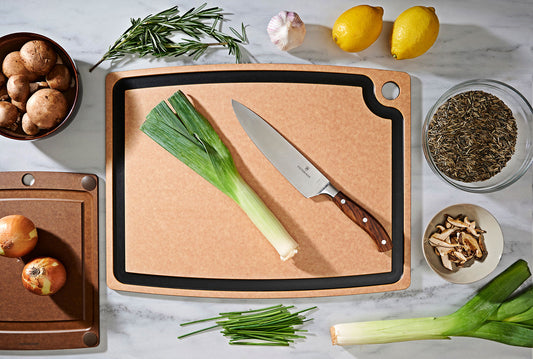 Natural slate cutting board with vegetables, herbs, and a knife on a countertop
