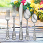 Five-piece floral-engraved flatware set on wooden table with blurred garden flowers.