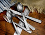 Angled close-up of utensils from the American Industrial 65-piece set showcasing the tumbled 18/10 stainless steel finish on a wooden table with burlap