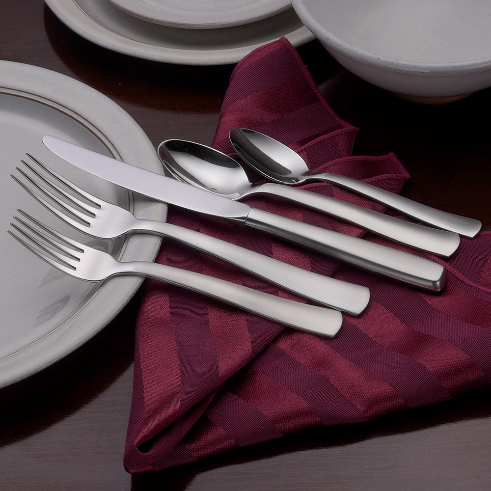 Satin America 65 Piece Set including forks, knives, and spoons on a table setting with plates and a napkin
