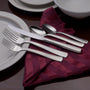 Angled view of Satin America 65-piece flatware showing satin brushed handles and hollow-handle knife on a folded burgundy napkin with white plates