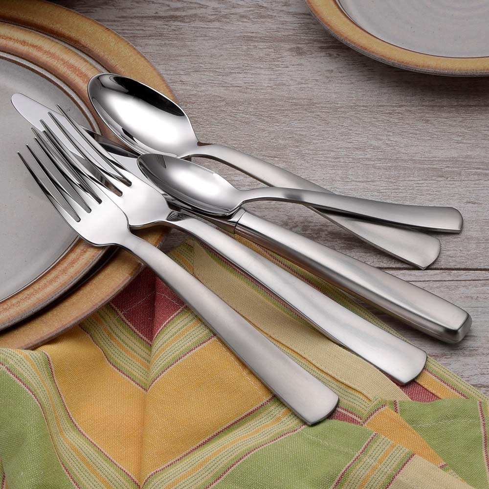 Stainless steel cutlery set displayed on a table with plates and a colorful tablecloth.