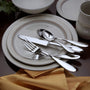 Top-down view of Betsy Ross flatware set showcasing mirror-finish teardrop handles on stacked ceramic plates with gold napkin