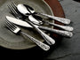 Angled view of Calavera flatware showing skull-motif handles on forks, spoons, and knives on a ceramic plate