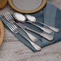 Angled view of Candra flatware showcasing brushed finish handles and mirror finish bowls on a blue napkin with plates