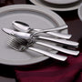 Angled view of Cedarcrest flatware showing parallel line pattern on forks, spoons, and knives on a white plate over a burgundy napkin