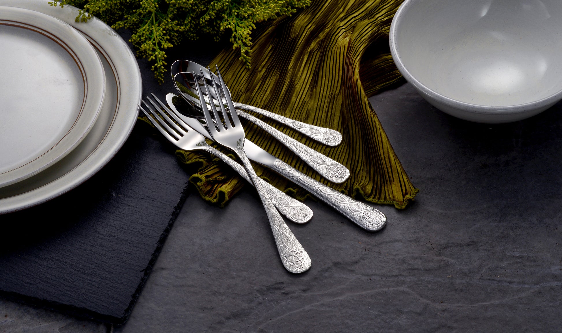 A set of silverware including forks and plates on a dark surface with green fabric.