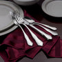 Polished silver forks and spoons arranged on a folded burgundy striped napkin beside stacked ceramic plates.