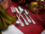 Angled view of five pieces from the Holidays flatware set showcasing ornate engraved handles on a red textured napkin with holiday decor