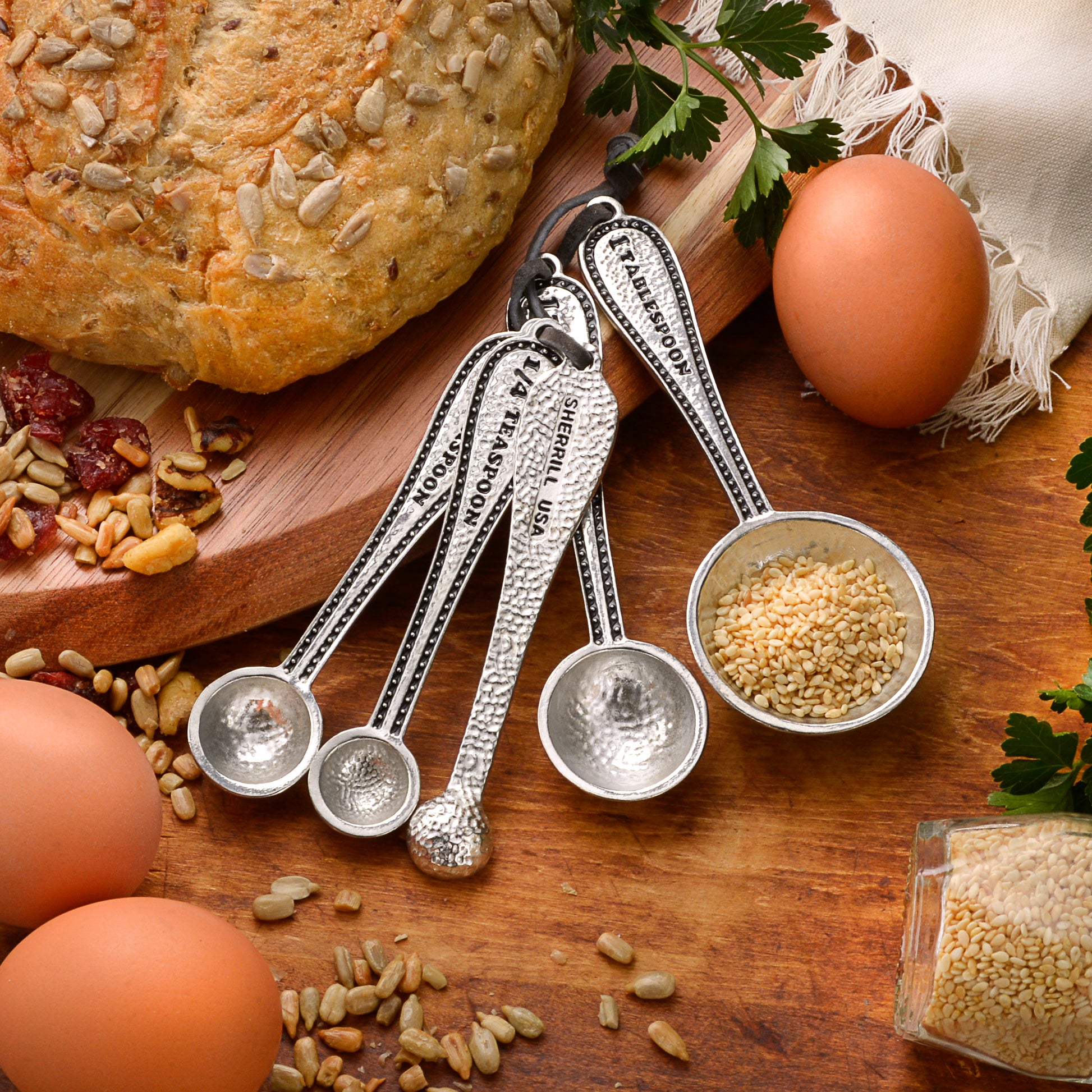 Set of measuring spoons with sesame seeds, eggs, and bread on a wooden surface