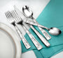Five-piece stainless steel flatware with floral-etched handles, arranged on a teal napkin beside a plate.