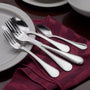 Stainless-steel flatware set (two forks, tablespoon, teaspoon) with beaded edges on a burgundy napkin beside a white plate
