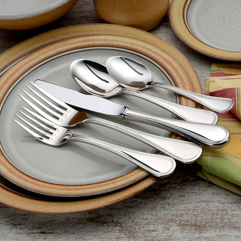 Five pieces of Pearl flatware set on plates, showcasing beaded design.