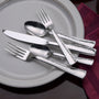 Top view of Pinehurst- 65 Piece Set showing hammered stainless-steel flatware on gray plate with burgundy napkin