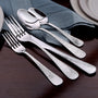 Hammered stainless flatware — two forks and two spoons arranged on a blue napkin beside stacked plates.