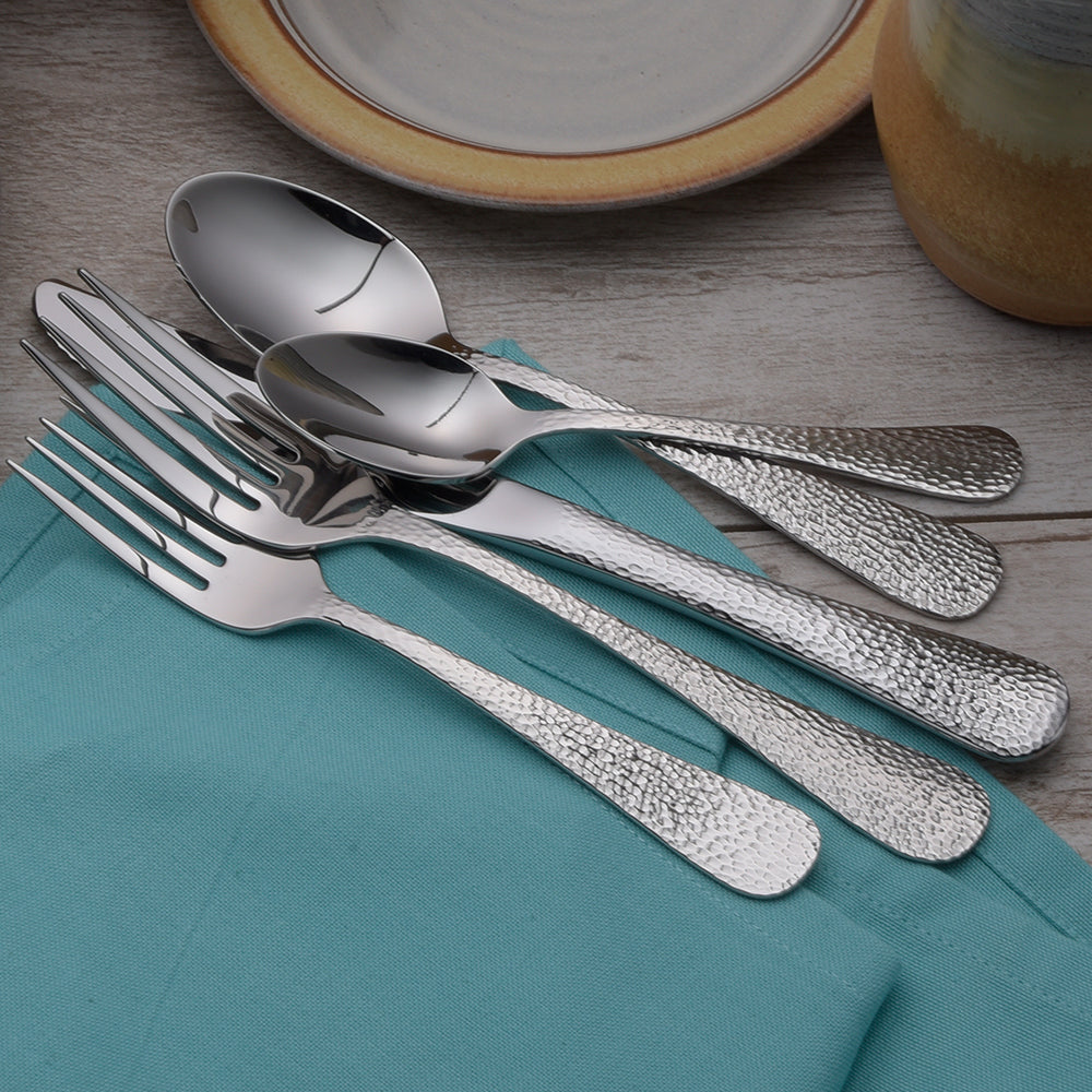 A set of silver utensils including forks, spoons, and knives on a teal napkin.