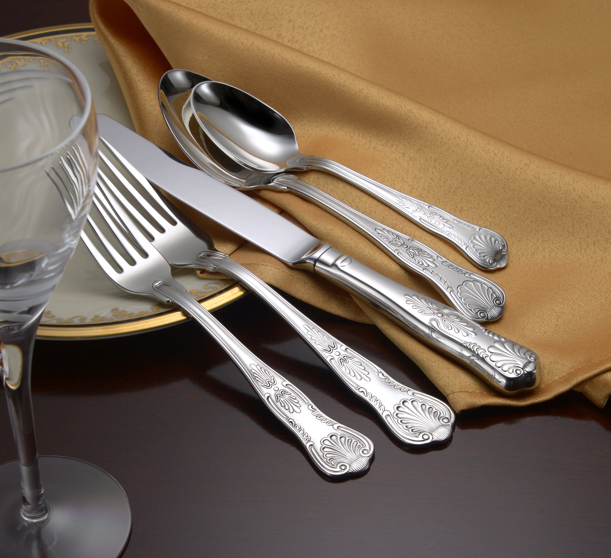 Silverware set including a fork, knife, spoon, and serving utensils on a gold tablecloth with a plate and glass.