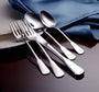 Angled view of polished stainless steel forks, spoons, and knife from Susanna flatware set on dark wood table with blue napkin