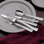 Angled view of Weave five-piece flatware showcasing woven-handle pattern on gray plate with burgundy napkin