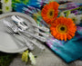 Angled view of Woodstock 45-piece flatware with ornate embossed peace and flower motifs on a plate and tie-dye cloth