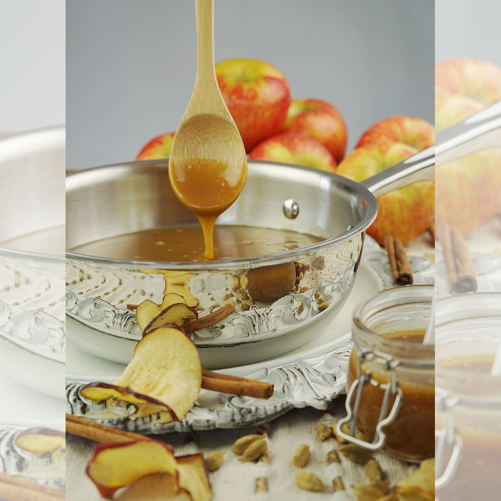 A 2-quart stainless steel saucier with caramel sauce, apples, and cinnamon sticks.